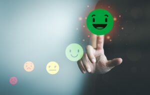 Afbeelding van een hand die een groene, lachende emoji aanraakt, omringd door andere emoji's die verschillende emoties uitdrukken, variërend van boosheid tot blijdschap.