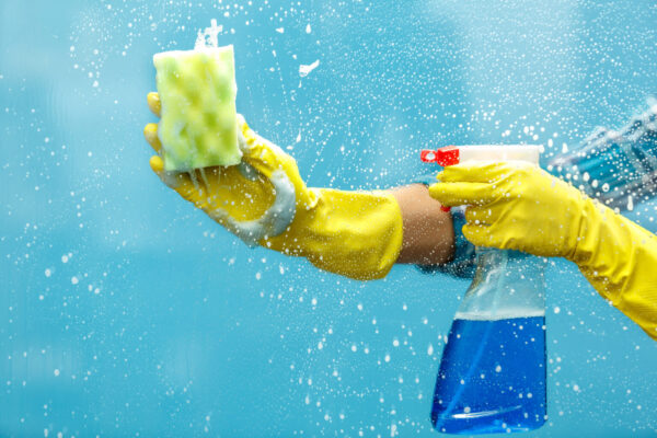 Een spons, handschoen en schoonmaakmiddel op een raam